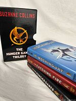 Photo showing the box set with the three hardcover books - Mockingjay (blue dust jacket), Catching Fire (red dust jacket) and The Hunger Games (black dust jacket) aligned side by side with the slipcase box.