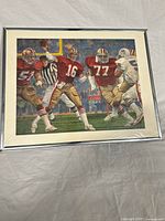 Full view of framed lithograph with original protective plastic, showing Joe Montana and other 49ers players on the football field during Super Bowl XIX.