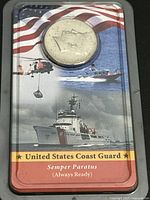 Kennedy half dollar coin in clear plastic casing with a background card featuring US Coast Guard ship, helicopter, and American flag.