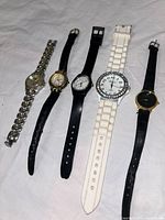 Five ladies wristwatches laid side by side showing bands and faces, various materials including metal, leather, and plastic, different dial designs.