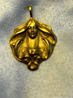 Close-up photo of the pendant showing the Art Nouveau style woman's face and hair in high relief gold tone metal.