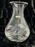 Full view of the clear crystal vase with etched leaf design around the bottom half, wide flared mouth, and heavy base, displayed on black fabric.