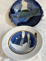 Pair of artisanal pottery bowls, one deep blue with handles, the other white with blue and brown abstract glaze