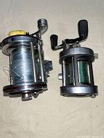 Pair of fishing reels, one larger vintage Millionaire reel with yellow handle knob, one smaller Penn model 49 reel with green fishing line.