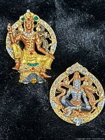 Pair of two ornate Thai Buddhist medallions styled as pins or pendants on a black background
