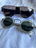 Two pairs of retro sunglasses on white fabric background, showing front view of both pairs.