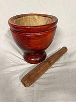 Front angled view of the wooden mortar and pestle shown on white background, highlighting the polished reddish finish of the mortar and natural wood color of the pestle.