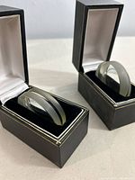 Two thick clear magnifying lenses displayed each inside separate black hinged boxes lined with white satin-like interior.