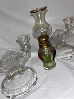 Pair of clear glass candlestick holders with fan-shaped back and twisted round bases visible beside mini oil lamp with colored glass and brass burner.