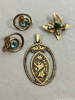 Three vintage jewelry pieces: MCM earrings, MCM pin, and bird pendant lying flat on a fabric surface.