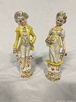 Male and female porcelain French colonial figurines with yellow and white clothing, gold accents, and detailed facial features.