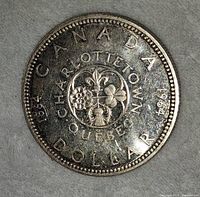Reverse of the 1964 Canadian silver dollar showing Charlottetown, Quebec Centennial floral design and inscriptions around the edge.