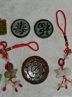 Photo of circular stone medallions with Chinese characters and a brown carved medallion featuring yin-yang symbol, along with red braided cord keychains with animal and bead charms.