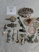 Photo showing assorted metal figurines including cityscape silhouette, musical instruments, angel dated 2000, animal figures, and other miniatures arranged on a flat surface