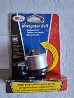 Front view of Bell Navigator Bell in original red and blue packaging showing the silver bell with integrated floating compass and branding details.