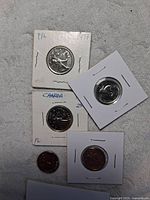 Photo showing five Canadian coins, mostly encapsulated, including 1967 nickels and quarters with visible dates and maple leaf design.