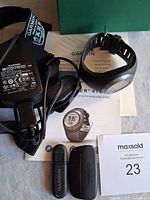 Garmin Forerunner 410 GPS running watch with charger, heart rate strap, USB dongles, manuals, and green storage box arranged on a surface.