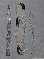 Full lot showing silver sterling 925 bracelet with rectangular links and Asian characters, a triple strand necklace with black and clear beads plus freshwater pearls and faux pearls, and pair of dangle/drop earrings with small beads.