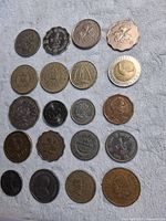 Top-down view of 20 mixed coins arranged in 4 rows showing various sizes, shapes, and designs including bi-metallic and scalloped edges.