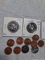 Two Canadian 50 cent coins in holders dated 1981 and 1983 with six 1 cent coins and three 5 cent coins below.