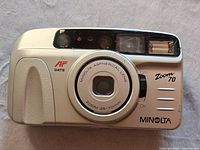 Front view of Minolta AF Zoom 70 camera showing lens, built-in flash, and front controls.