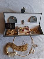 Jewelry box open showing assorted jewelry inside including a gold-tone tassel necklace prominently in front.