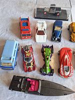 Close-up view of several die-cast toy vehicles including fire truck, white vintage car, blue sedan, and red racing cars, highlighting details and condition.