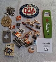 Photo showing all 20 items on white cloth background including pins, badge, cufflinks, tie clip, bottle opener, and keychain