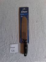 Full view of Oster Granger Santoku knife in original packaging showing the black handle and metal blade.