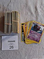 Two large stacks of Pokemon cards bundled with rubber bands and a smaller pile of loose cards with various Pokemon visible on top.