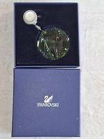 Swarovski navy blue box opened showing green crystal ornament paperweight and SCS seal inside.