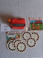 Red View-Master viewer, 6 reels with 3D images, and 2 packet covers displayed on neutral background