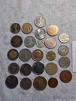 Top view of 25 assorted world coins on a grey surface showing variety in size, shape, metal color and designs.