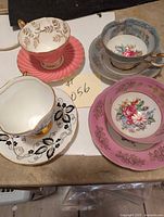 Four vintage teacups with matching saucers showing various floral and gold designs, placed on a table surface.