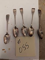 Top view of 5 silver spoons arranged in a row showing their shape and size with a note #055 included.