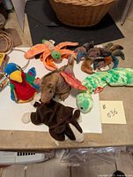 Six assorted Beanie Babies plush toys displayed on a table including a parrot, spider, elephant, snake, and two frogs with visible Ty tags.