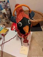 Front view of cardinal ornament showing red mesh fabric body, black face, orange beak, blue and orange earmuffs, googly eyes, and part of electrical cord.