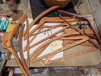 Photo showing 14 vintage wooden clothes hangers with metal hooks on a table, some branded with business names.