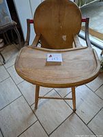Front view of the old wooden high chair showing the tray, seat, and armrests with red paint.