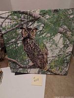 Full view of square canvas with owl perched on tree branch with detailed feathers and green leaves around.