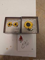 Photo shows sunflower earrings and sunflower brooch on branded backing cards inside separate boxes, labeled 'Canadian Naturals by Hinterland' and indicating handmade leather items.