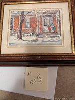 Framed picture showing a winter scene of a woman and child on a snowy porch in front of a brick house.