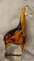 Side view of amber glass giraffe figurine showing amber body with black spots and clear glass base.