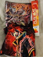 Anime hoodie with red and black design and fox mask character, and Ultimate Guard box with playmat visible