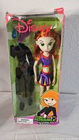 Front view of Disney Kim Possible fashion doll in original green box, showing doll with purple outfit and accessory outfit visible behind.