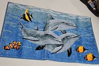 Top view of the bath mat showing the front side with three dolphins and tropical fish on a blue water background.