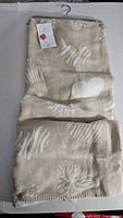 Folded beige plush blanket on hanger with tags, showing overall color and pattern.