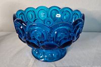 Front side view showing the textured circular and starburst Moon and Stars pattern with scalloped rim on the blue glass compote bowl.