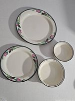 Lenox dinnerware pieces with pink floral designs and dark rims including plates and bowls laid flat on a light surface.