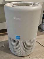 Front view of white Levoit air purifier showing logo and ventilation holes on cylindrical body.